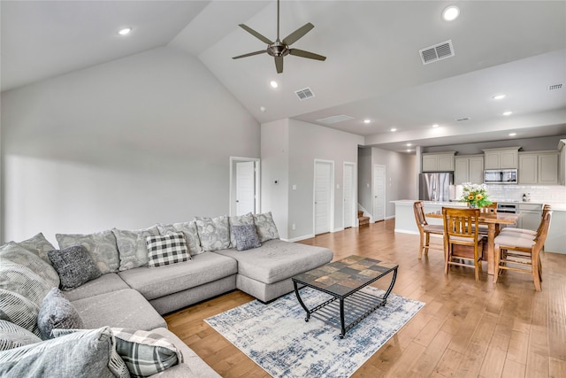 living area with high vaulted ceiling, light wood-type flooring, visible vents, and stairs