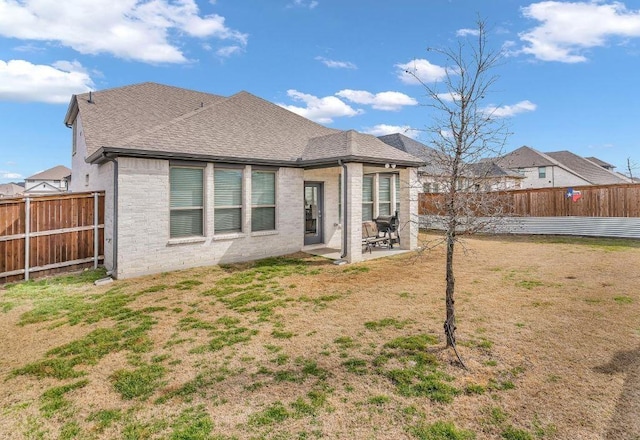 back of property with a patio, a fenced backyard, brick siding, a shingled roof, and a yard