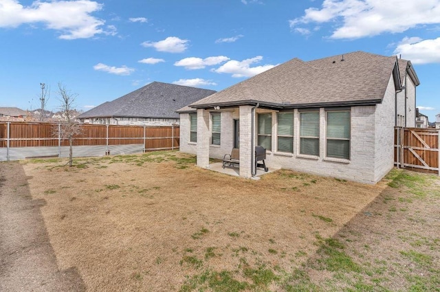 rear view of property with a patio area, brick siding, a fenced backyard, and roof with shingles