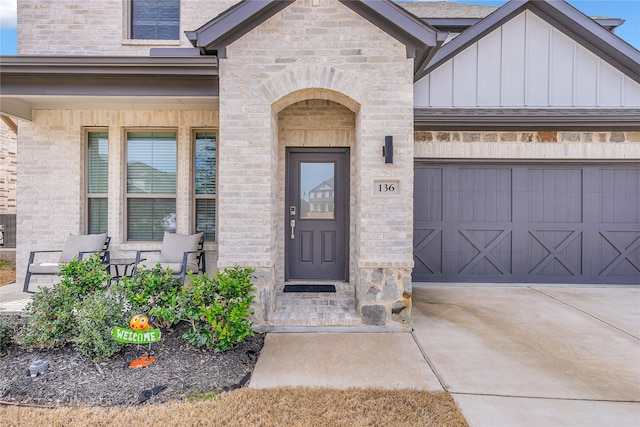 property entrance featuring a porch, concrete driveway, an attached garage, board and batten siding, and stone siding