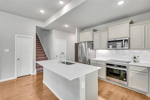 kitchen featuring stainless steel appliances, a sink, light wood-style flooring, and decorative backsplash