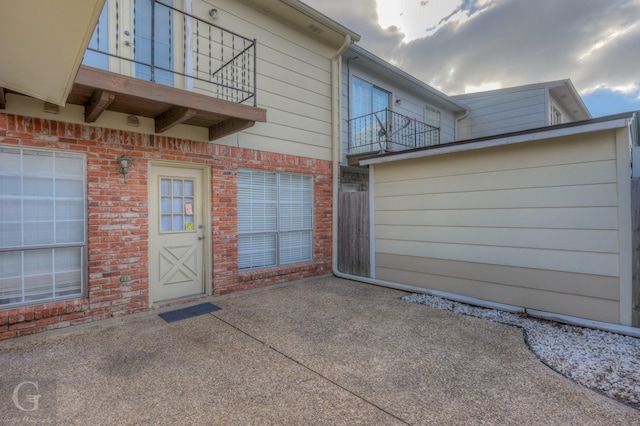 view of exterior entry featuring brick siding, a patio, and a balcony