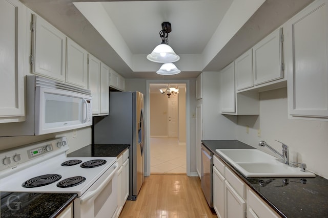 kitchen featuring a tray ceiling, pendant lighting, white cabinets, a sink, and white appliances