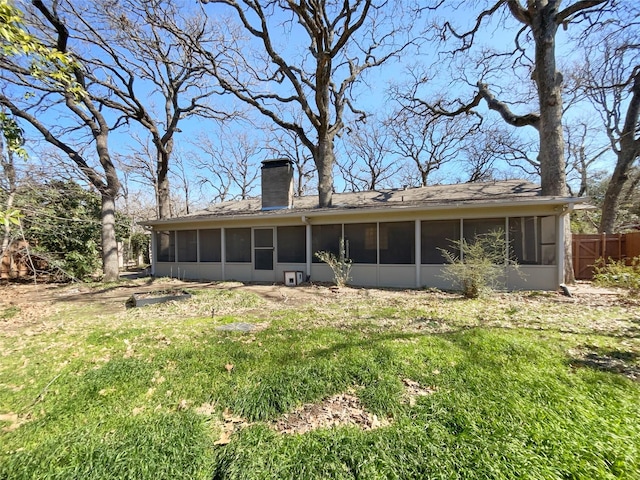 back of house with a sunroom, a chimney, fence, and a lawn