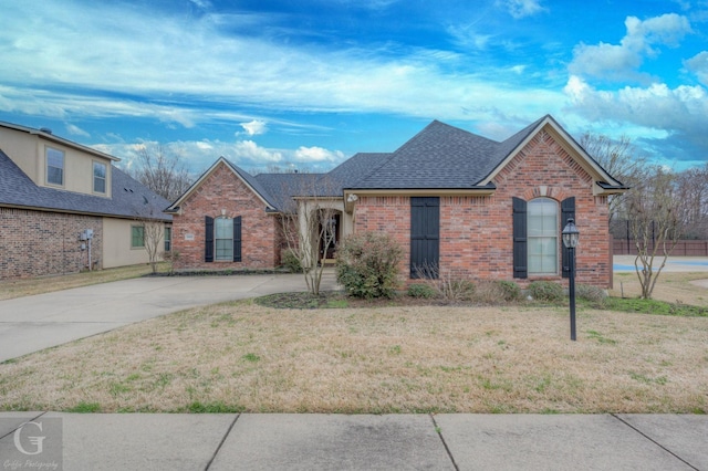 view of front of house featuring driveway, a shingled roof, a front yard, and brick siding