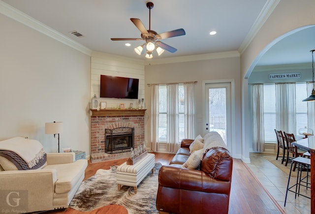 living area featuring ornamental molding, arched walkways, a brick fireplace, and light wood-style flooring