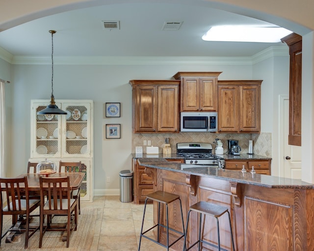 kitchen with arched walkways, stainless steel appliances, visible vents, hanging light fixtures, and brown cabinetry