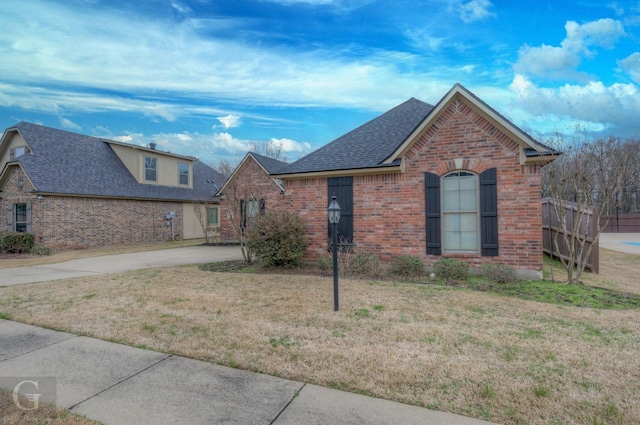 view of front of house featuring a shingled roof, a front yard, and brick siding