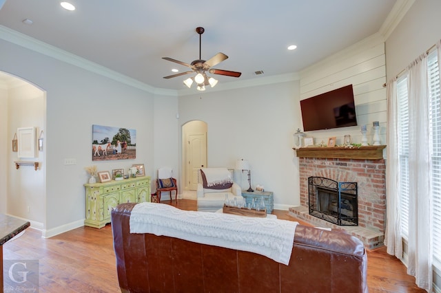 living area featuring arched walkways, a brick fireplace, crown molding, and wood finished floors