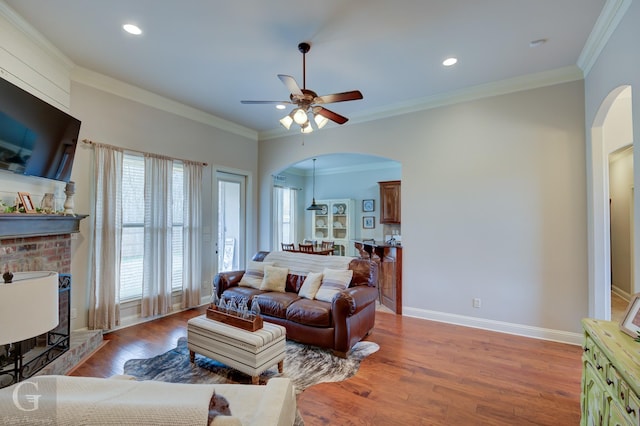 living area featuring arched walkways, baseboards, wood finished floors, and crown molding