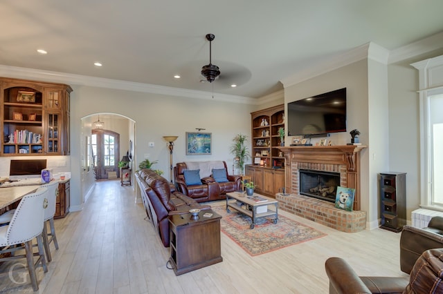 living room featuring arched walkways, french doors, a fireplace, light wood finished floors, and ornamental molding