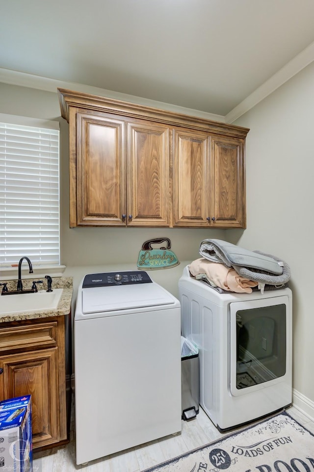 washroom with ornamental molding, washer and clothes dryer, a sink, and cabinet space