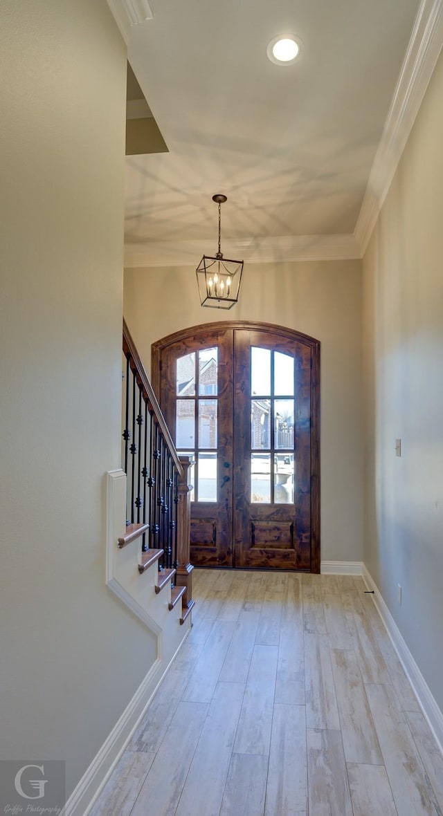 entryway with an inviting chandelier, stairs, crown molding, french doors, and light wood-type flooring