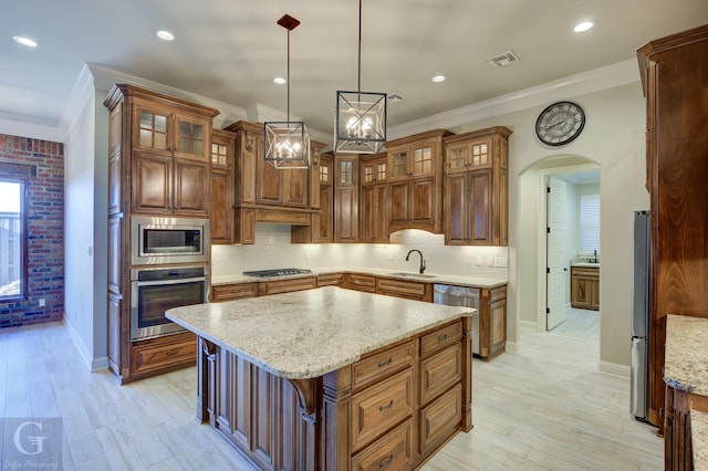 kitchen featuring hanging light fixtures, appliances with stainless steel finishes, glass insert cabinets, a sink, and a kitchen island