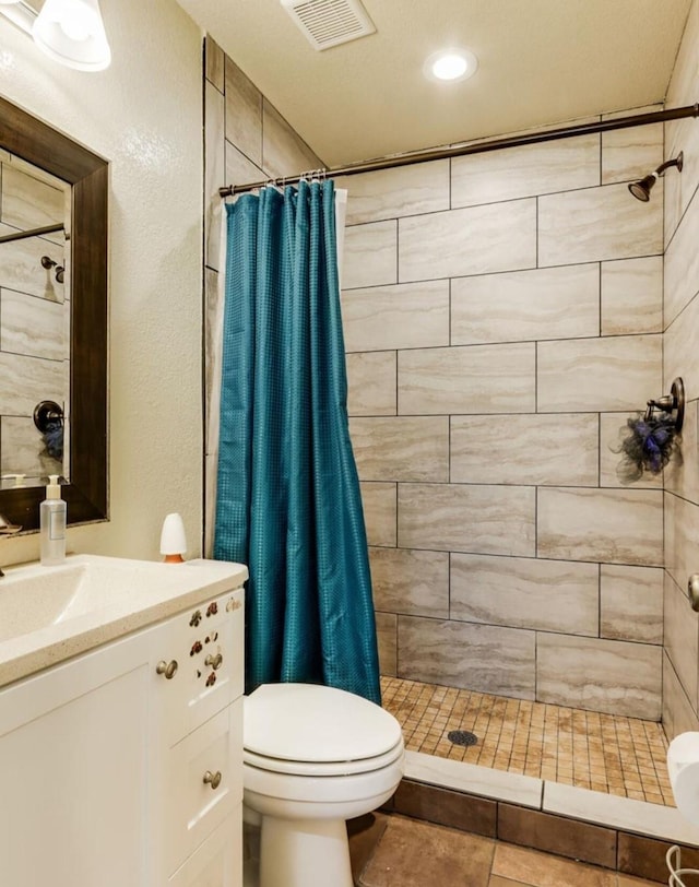 full bath featuring toilet, vanity, a tile shower, and visible vents