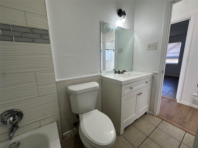 full bathroom with a wainscoted wall, tile walls, toilet, vanity, and tile patterned floors