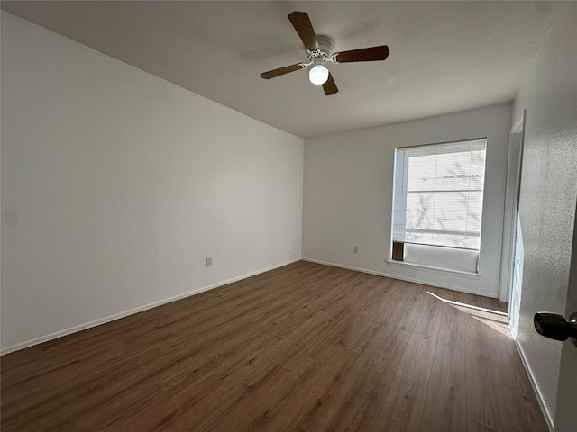 spare room featuring dark wood-style floors, a ceiling fan, and baseboards