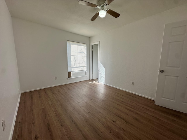 empty room with ceiling fan, baseboards, and dark wood-type flooring