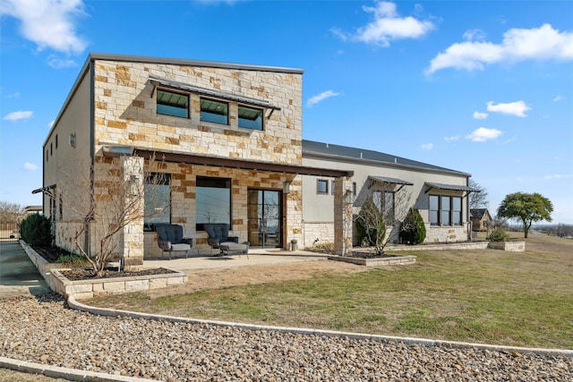 back of property with stone siding, a lawn, and a patio