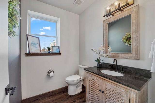 half bathroom featuring toilet, vanity, wood finished floors, and visible vents