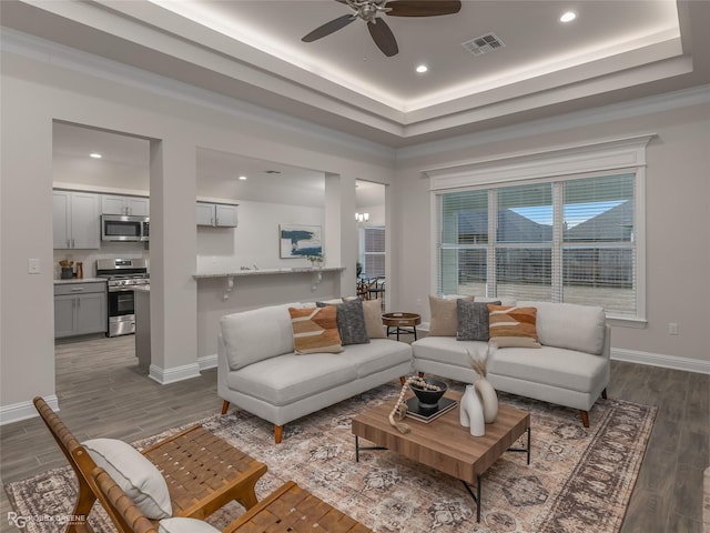 living area with a tray ceiling, visible vents, baseboards, and wood finished floors