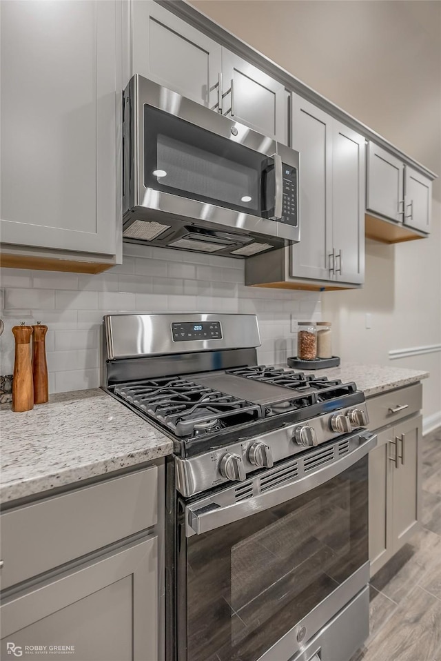 kitchen with light stone countertops, gray cabinets, stainless steel appliances, and decorative backsplash