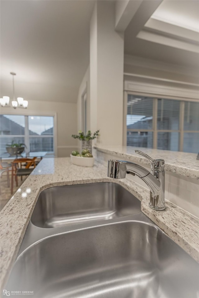 interior details with light stone countertops, an inviting chandelier, a sink, and decorative light fixtures