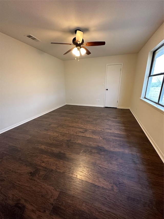 empty room featuring dark wood-style flooring, visible vents, ceiling fan, and baseboards