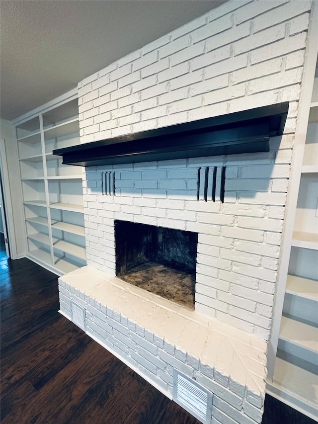 room details with a brick fireplace, a textured ceiling, built in shelves, and wood finished floors