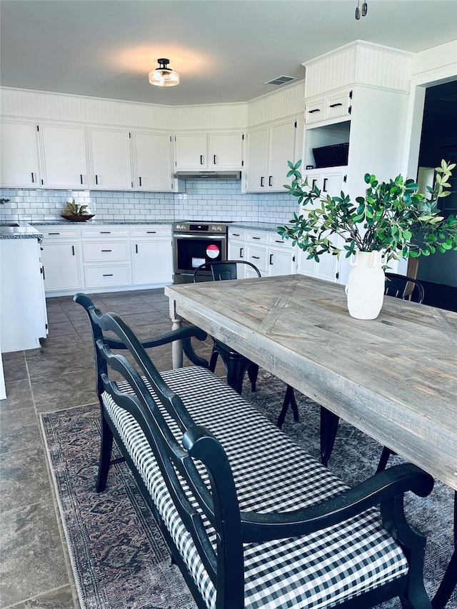 kitchen with under cabinet range hood, backsplash, stainless steel range with electric stovetop, and white cabinets