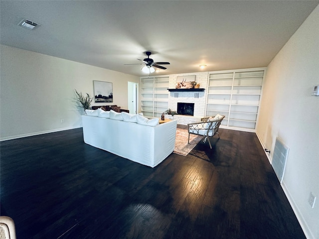 living room featuring dark wood-style flooring, a brick fireplace, visible vents, and a ceiling fan