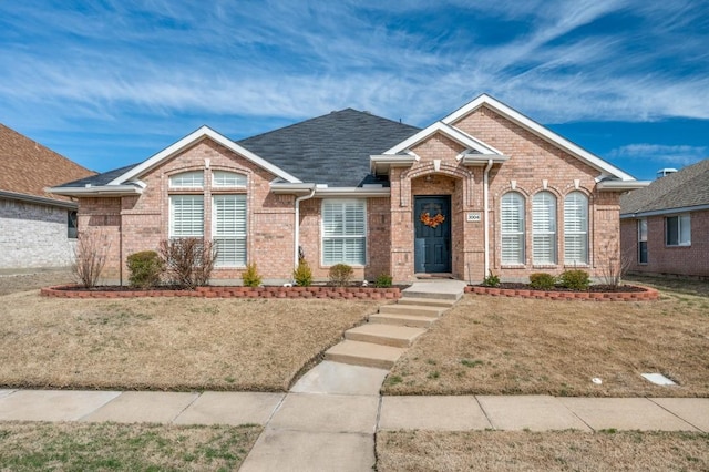 view of front facade with a shingled roof, a front yard, and brick siding