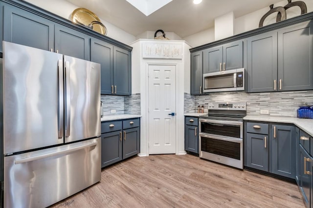 kitchen with a skylight, stainless steel appliances, backsplash, blue cabinets, and light wood-type flooring