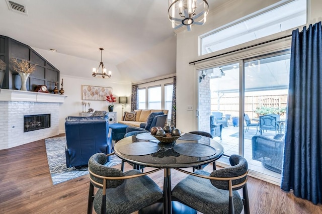 dining space featuring visible vents, a fireplace, a chandelier, and wood finished floors