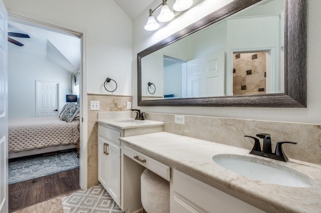 ensuite bathroom with tiled shower, lofted ceiling, ensuite bathroom, tile patterned flooring, and vanity