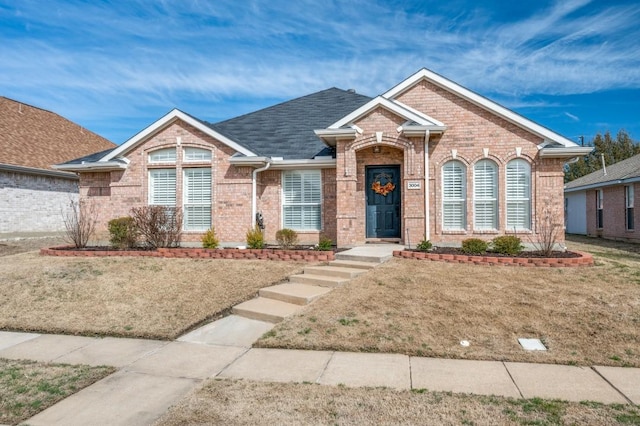 ranch-style house with brick siding, roof with shingles, and a front yard