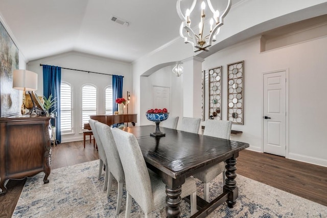 dining area featuring a notable chandelier, visible vents, vaulted ceiling, wood finished floors, and baseboards