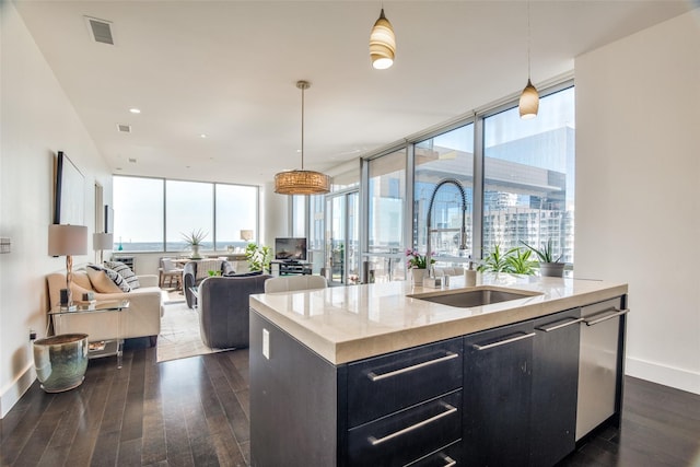 kitchen featuring an island with sink, light stone counters, open floor plan, hanging light fixtures, and a sink