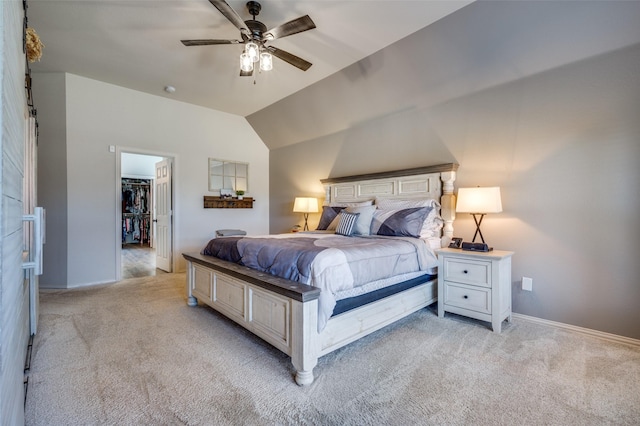 bedroom with a walk in closet, ceiling fan, baseboards, light colored carpet, and vaulted ceiling