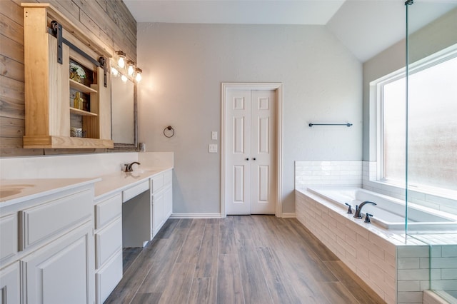 bathroom with wood finished floors, lofted ceiling, double vanity, a sink, and a garden tub