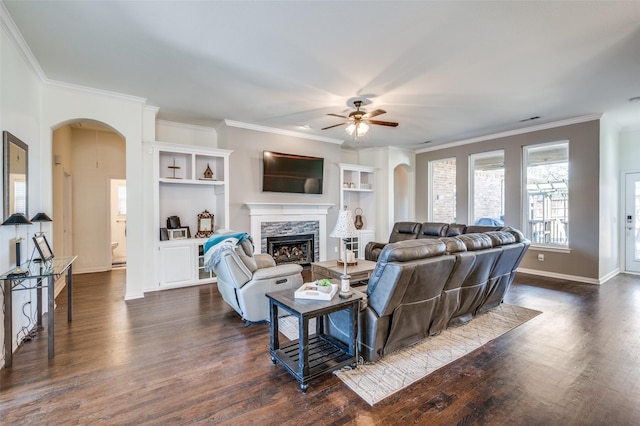 living area with arched walkways, a stone fireplace, dark wood finished floors, and a ceiling fan