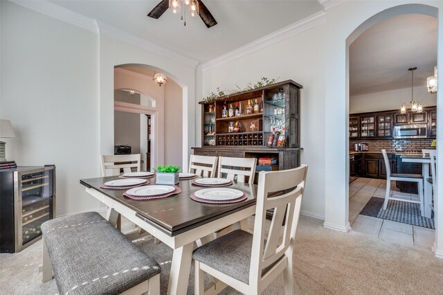 dining space featuring wine cooler, light colored carpet, ornamental molding, and arched walkways