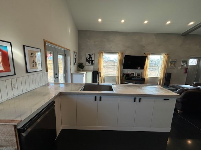 kitchen featuring black dishwasher, white cabinets, open floor plan, light countertops, and a sink