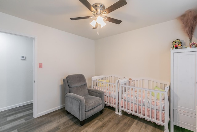 bedroom featuring a nursery area, dark wood finished floors, baseboards, and ceiling fan