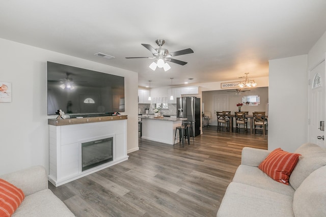 living room featuring dark wood-style floors, a glass covered fireplace, visible vents, and ceiling fan