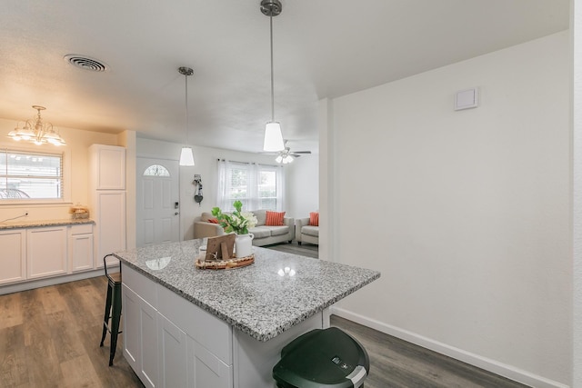 kitchen featuring visible vents, a breakfast bar, decorative light fixtures, a center island, and white cabinetry