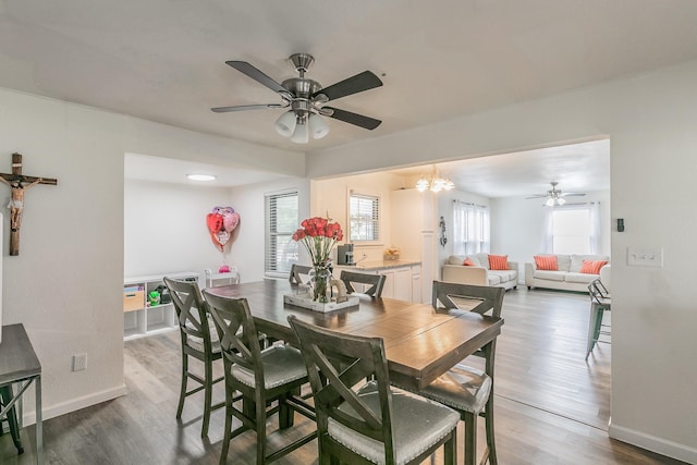 dining space with ceiling fan with notable chandelier, baseboards, and wood finished floors