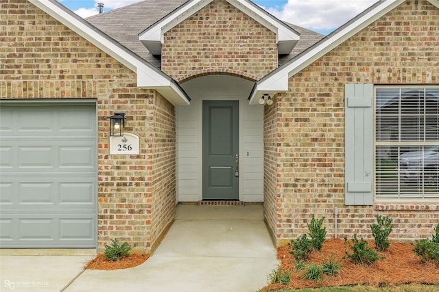 doorway to property with brick siding, an attached garage, and roof with shingles