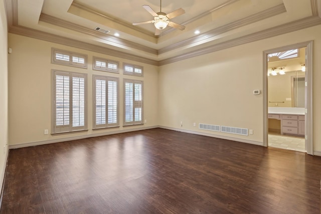 empty room featuring a tray ceiling, dark wood-type flooring, and visible vents