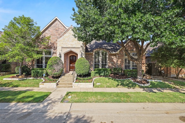 view of front of home featuring a front yard, stone siding, and brick siding